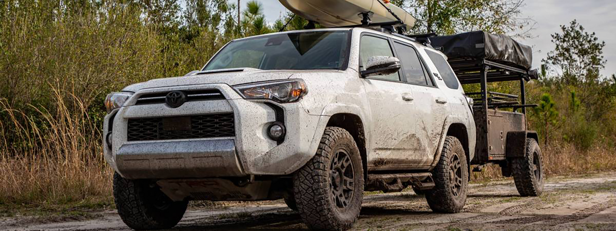 5th Gen Toyota 4Runner with roof rack and cargo trailer on gravel forest road