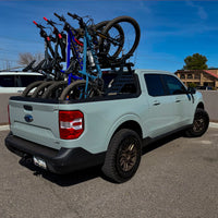 A bike rack mounted on the bed of a light blue pickup truck, holding several bicycles.