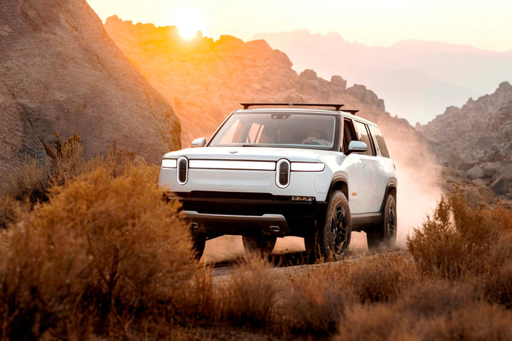 Rivian R1T on dirt track with dust during sunset