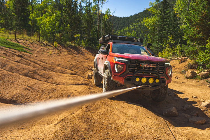Red GMC Canyon with a roof rack and front winch, winch line pulled tight on a dirt trail in the mountains