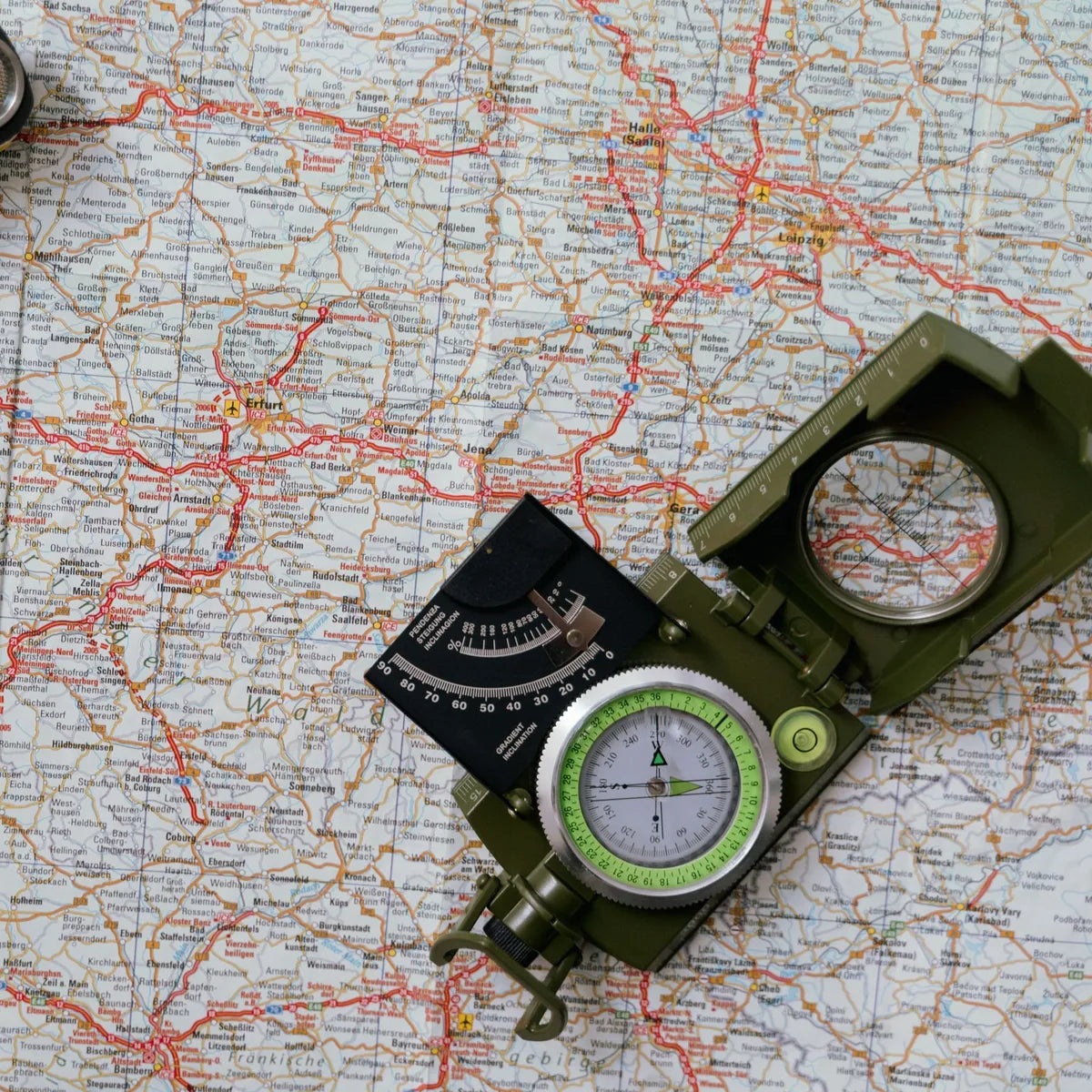 Lensatic compass with its cover open lying on a folded road map