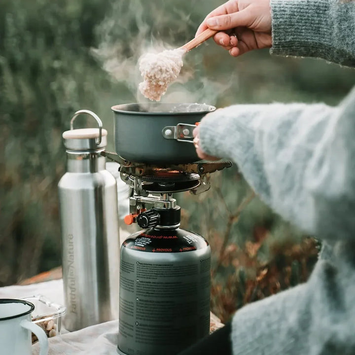 Pouring water into a pot on a canister stove next to an insulated bottle