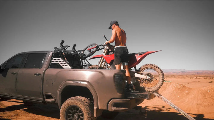 Rider loading a dirt bike onto a rack in a pickup truck bed