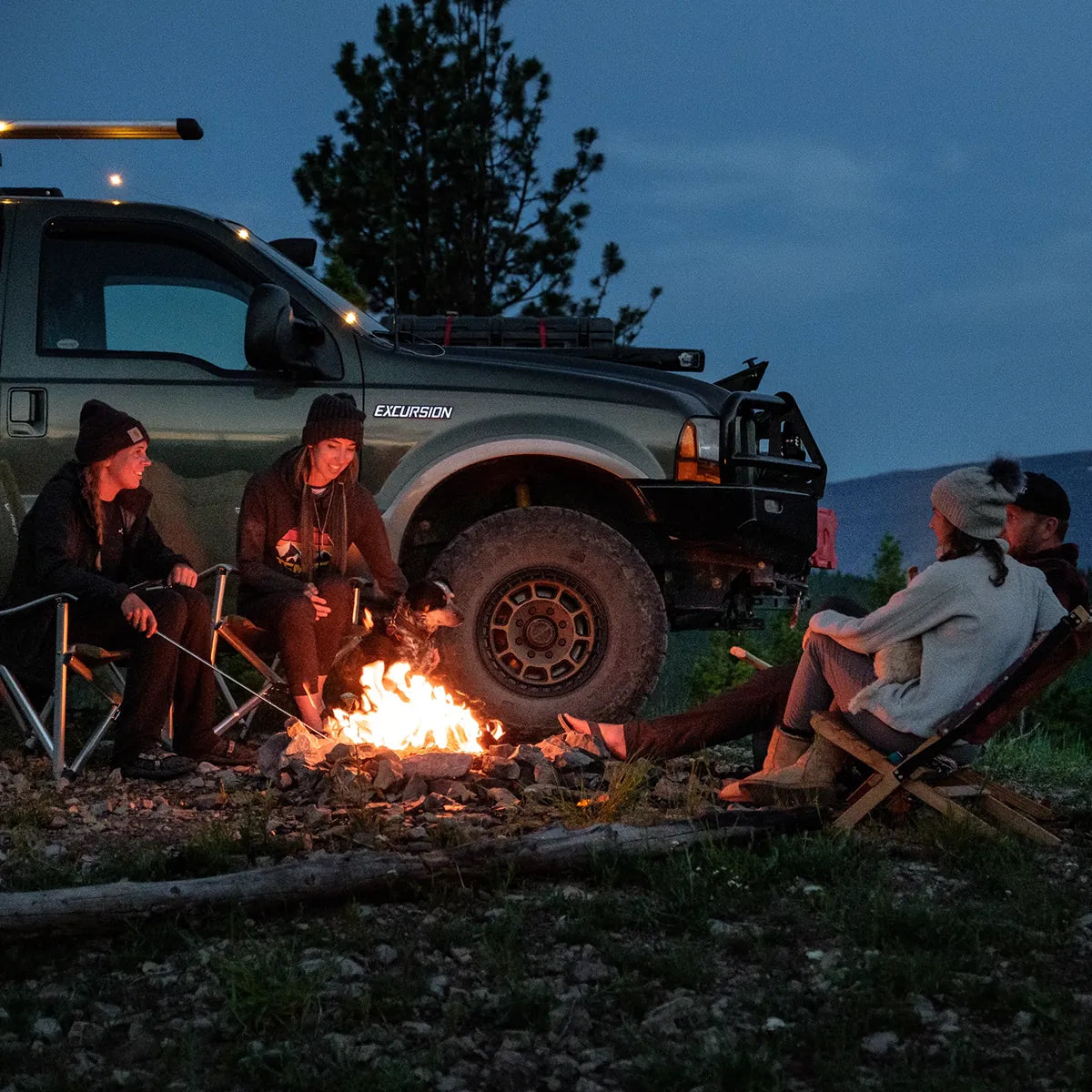 Group sitting around a campfire beside a parked truck at dusk
