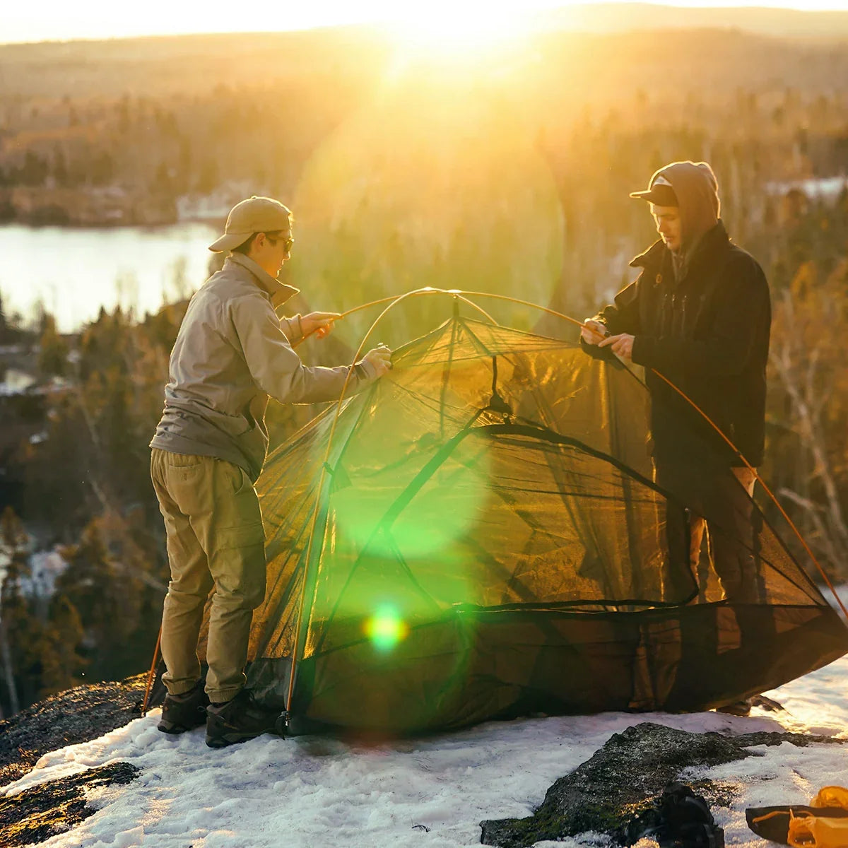 Two campers pitching a tent in the snow at sunrise