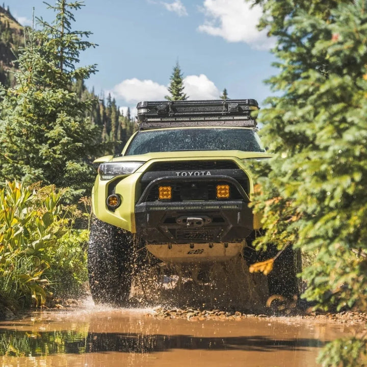 Lime green 5th Gen Toyota 4Runner with a CBI Covert front bumper and a roof rack splashing through a creek on a forest trail