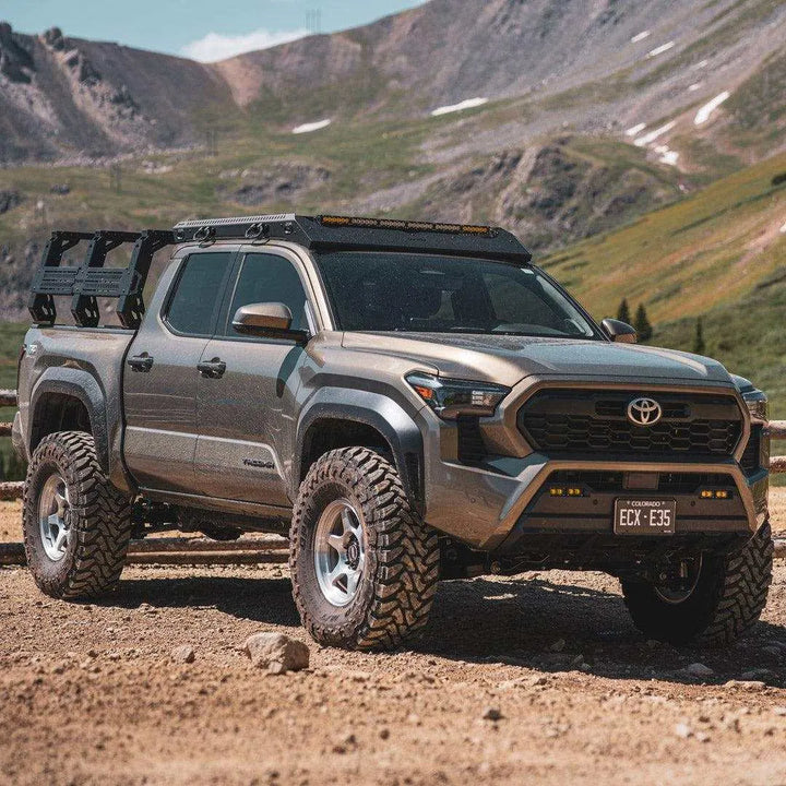 Gray Toyota Tacoma with a black upTOP TRUSS bed rack and a roof rack, parked on a dirt road in the mountains