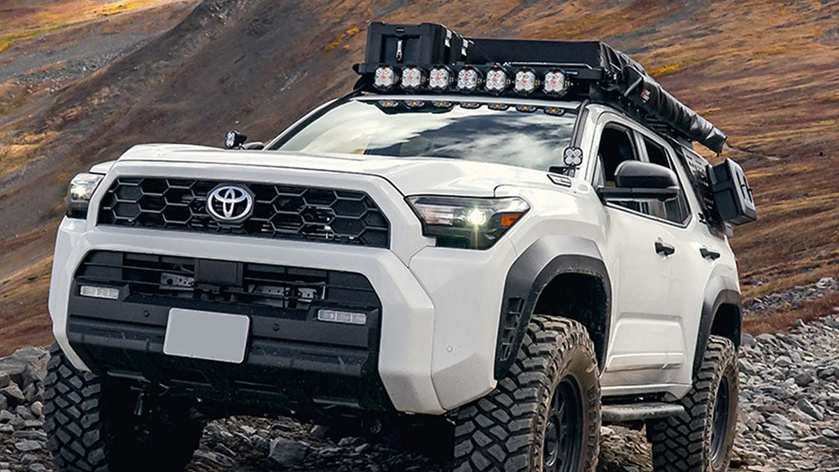 White 6th Gen Toyota 4Runner with a Front Runner Slimline II roof rack and LED light bar on a rocky mountain trail