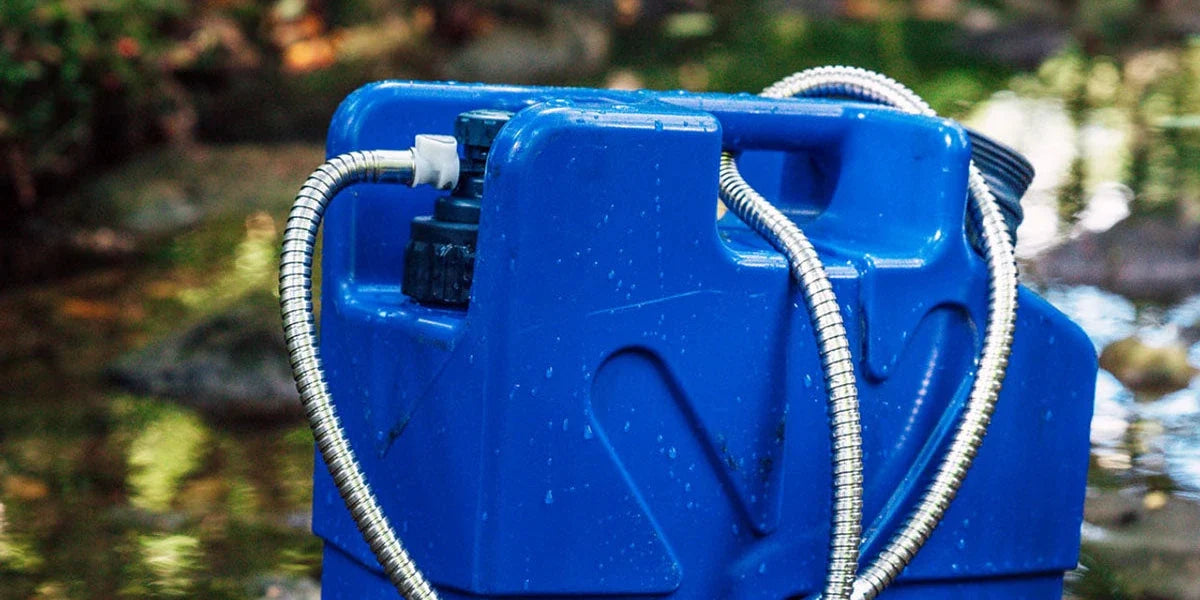 Blue LifeSaver Jerrycan water filter with the shower attachment hose, standing in a shallow creek