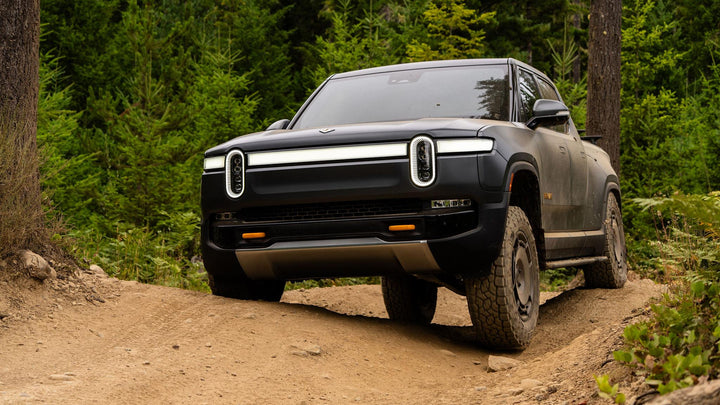 Black Rivian offroad, negotiating uneven track