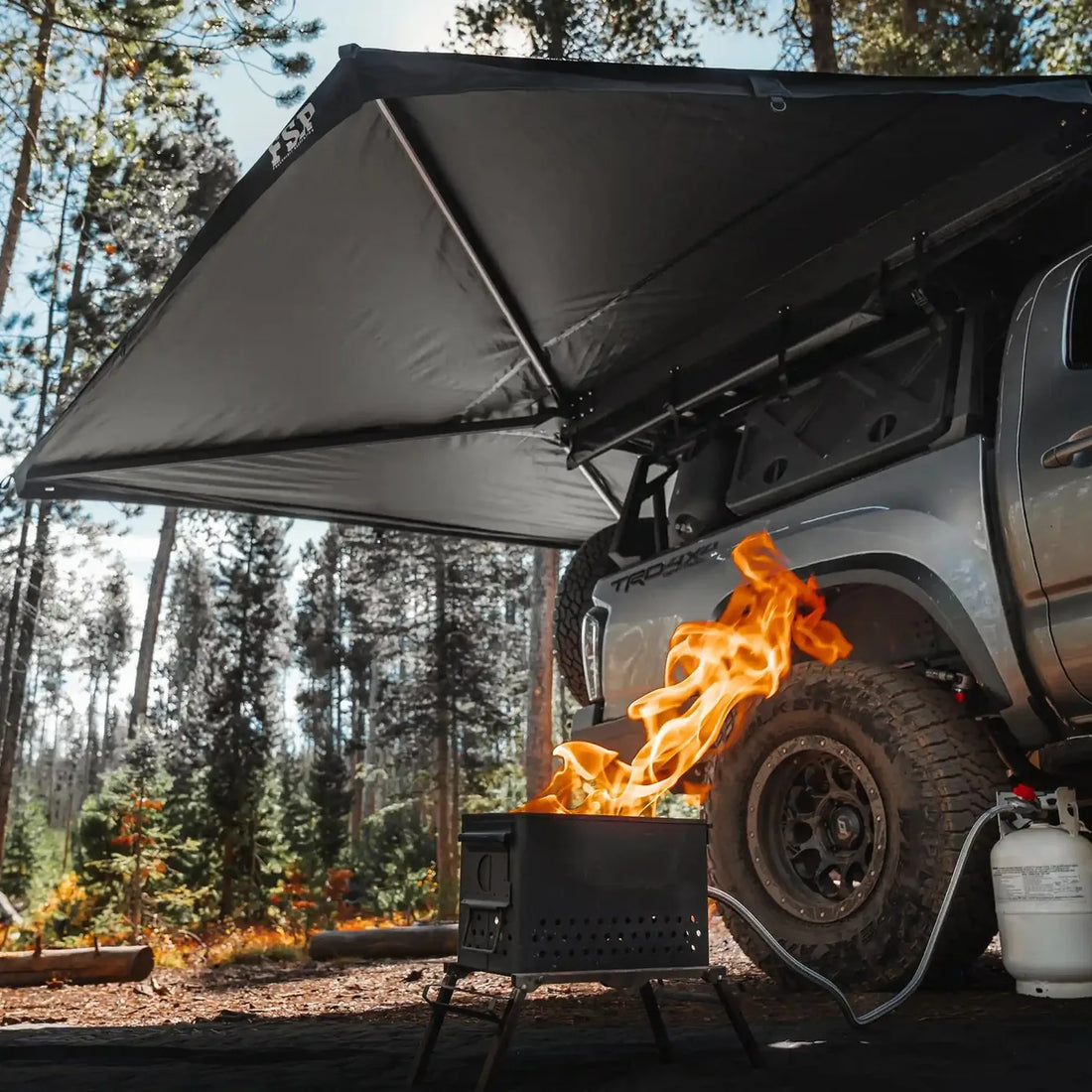 Free Spirit 270 Awning V2 deployed on a Tacoma at a forest campsite with a fire pit