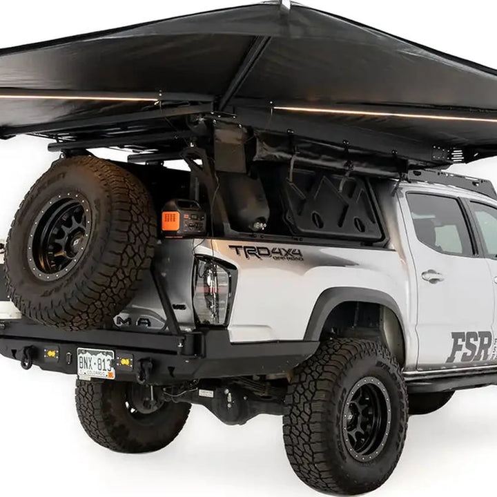 Free Spirit 270 Awning V2 deployed on a Tacoma at a forest campsite with a fire pit