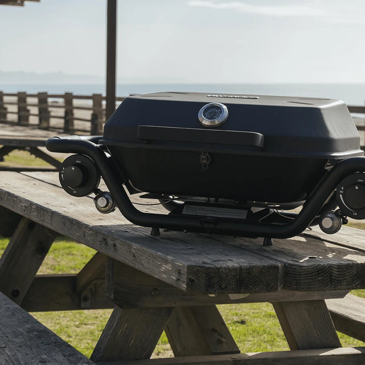 Portable grill on a wooden picnic table with a scenic background