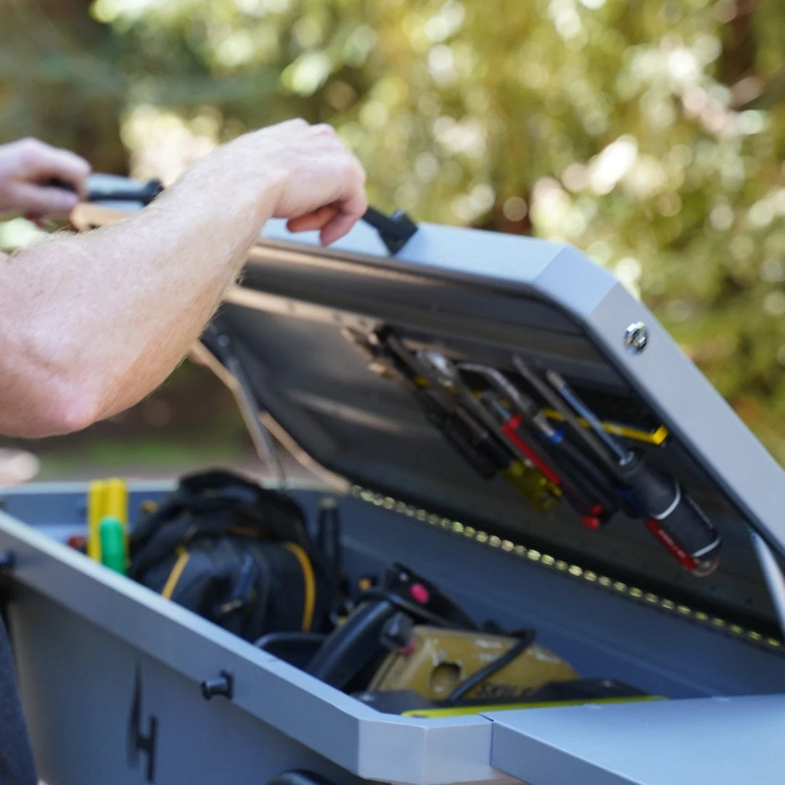 Person opening a tool box with tools inside, outdoors.