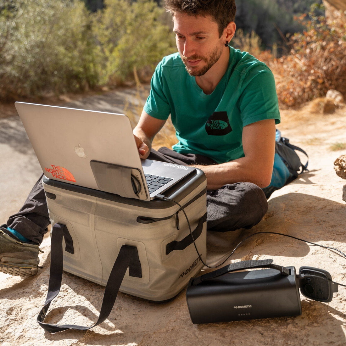 Man using a laptop on a large insulated bag outdoors