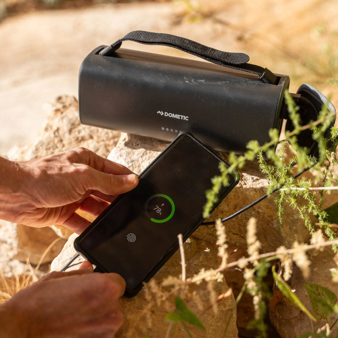 Person using a smartphone to charge a Dometic portable power station outdoors.