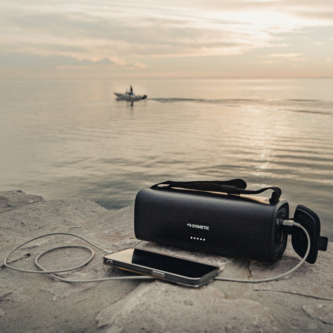 Black portable battery and smartphone on a rock with a boat in the distance on water.