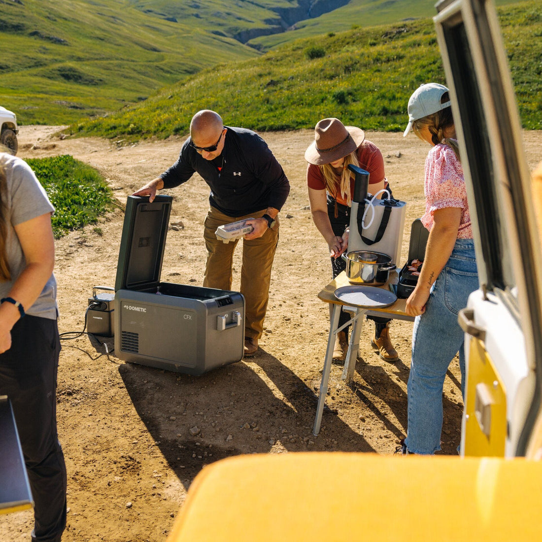Group of people preparing food outdoors near a vehicle in a natural setting