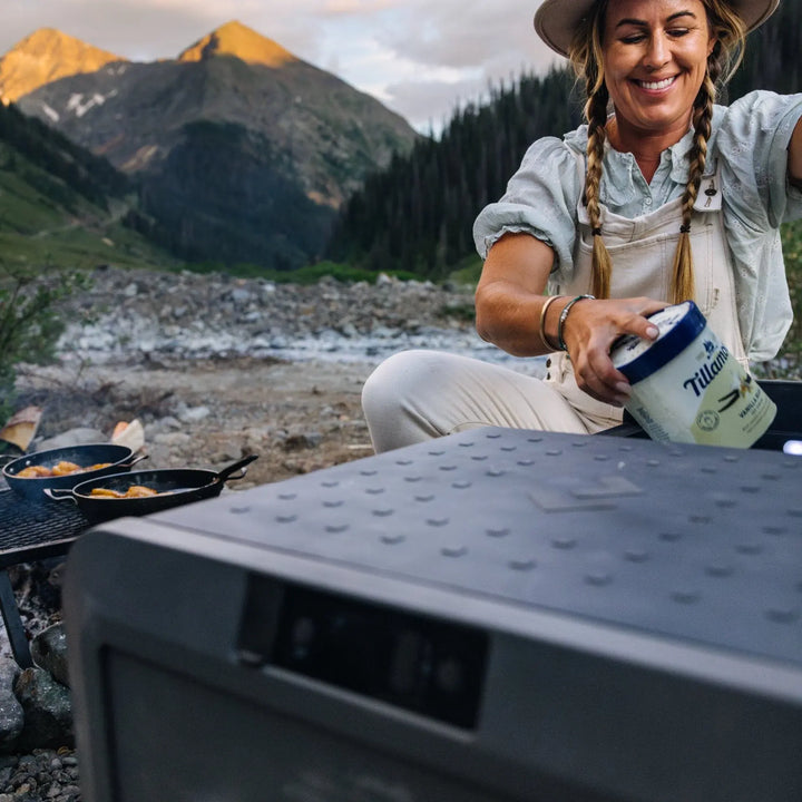 Dometic CFX5 95DZ dual zone cooler at a mountain campsite, opened by a camper
