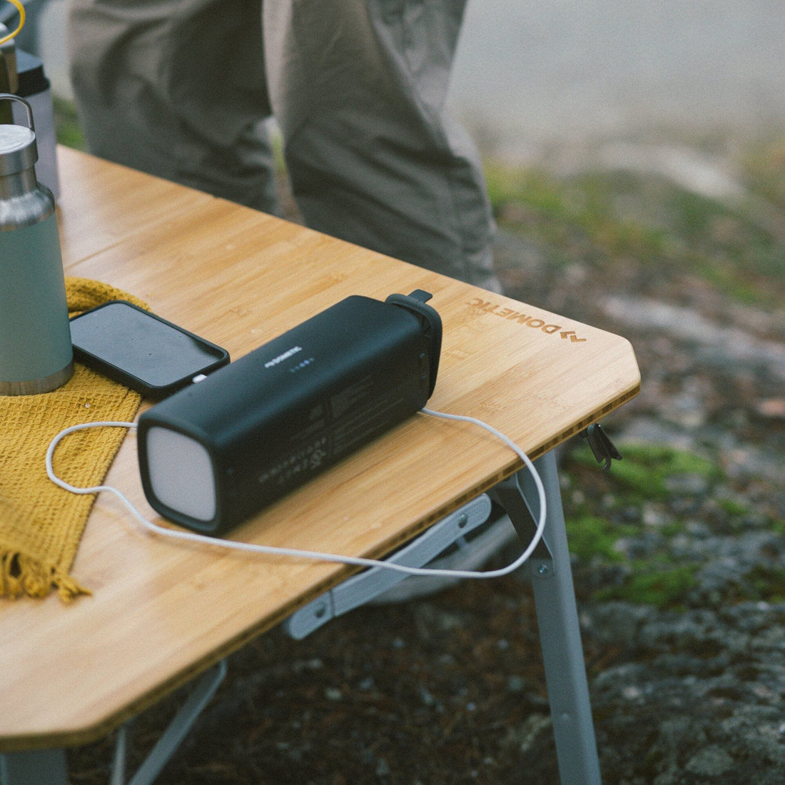 Portable battery pack charging a phone on a wooden table outdoors.