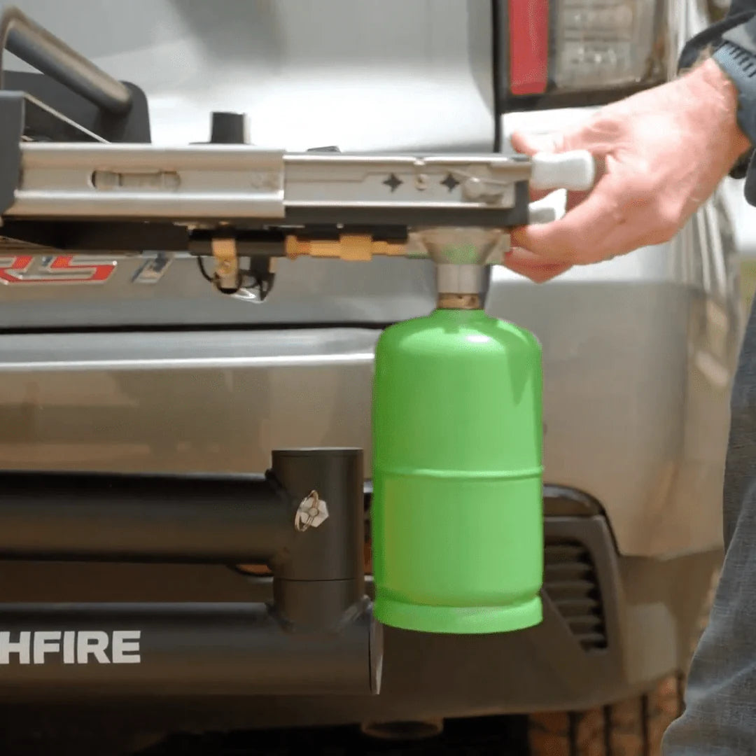 Person attaching a green propane tank to a HitchFire device on a vehicle
