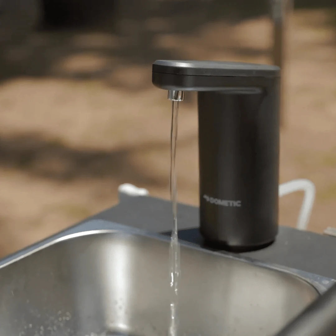 Black soap dispenser on a sink with water flowing, outdoor setting