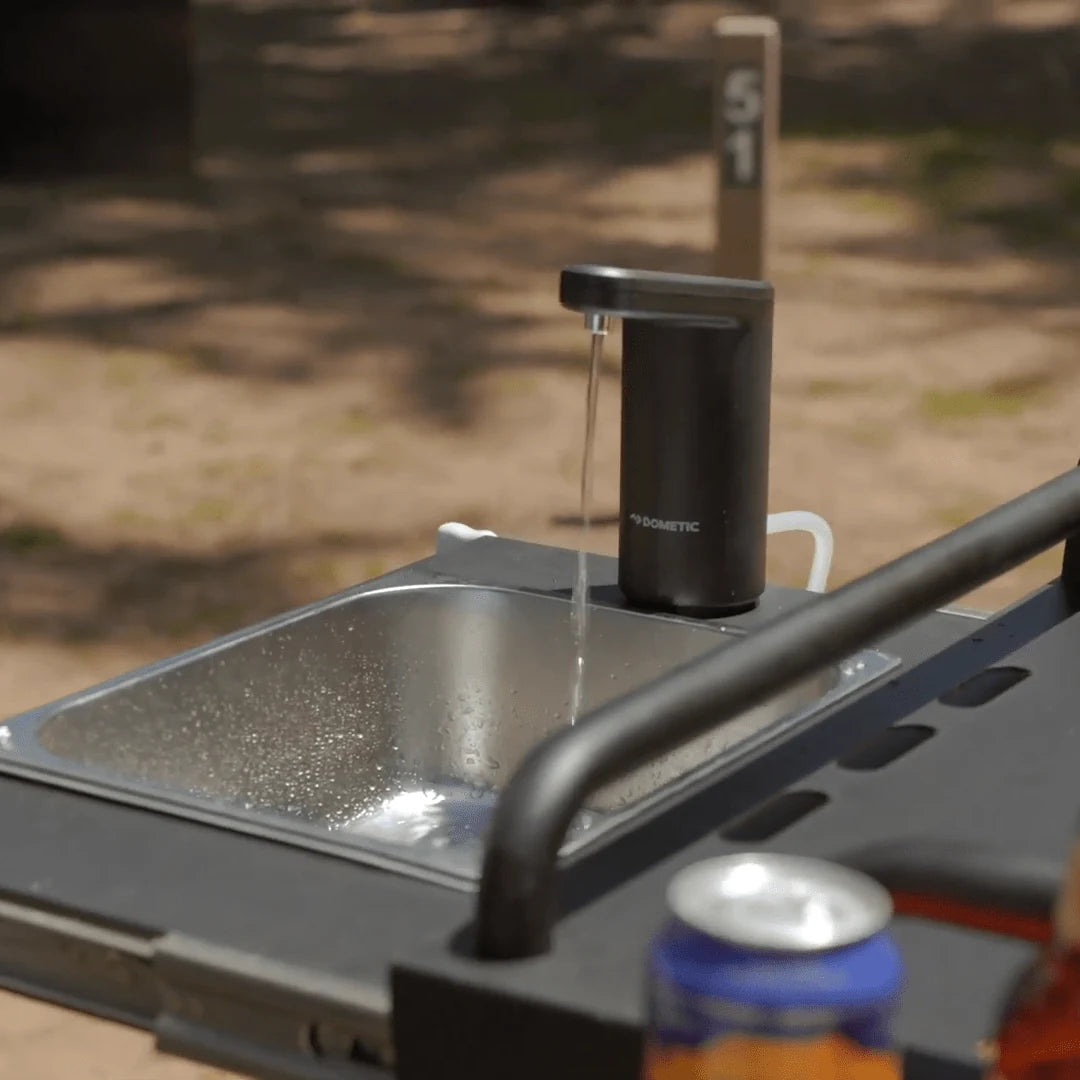 Portable outdoor kitchen sink with water flowing, surrounded by bottles on a natural background.