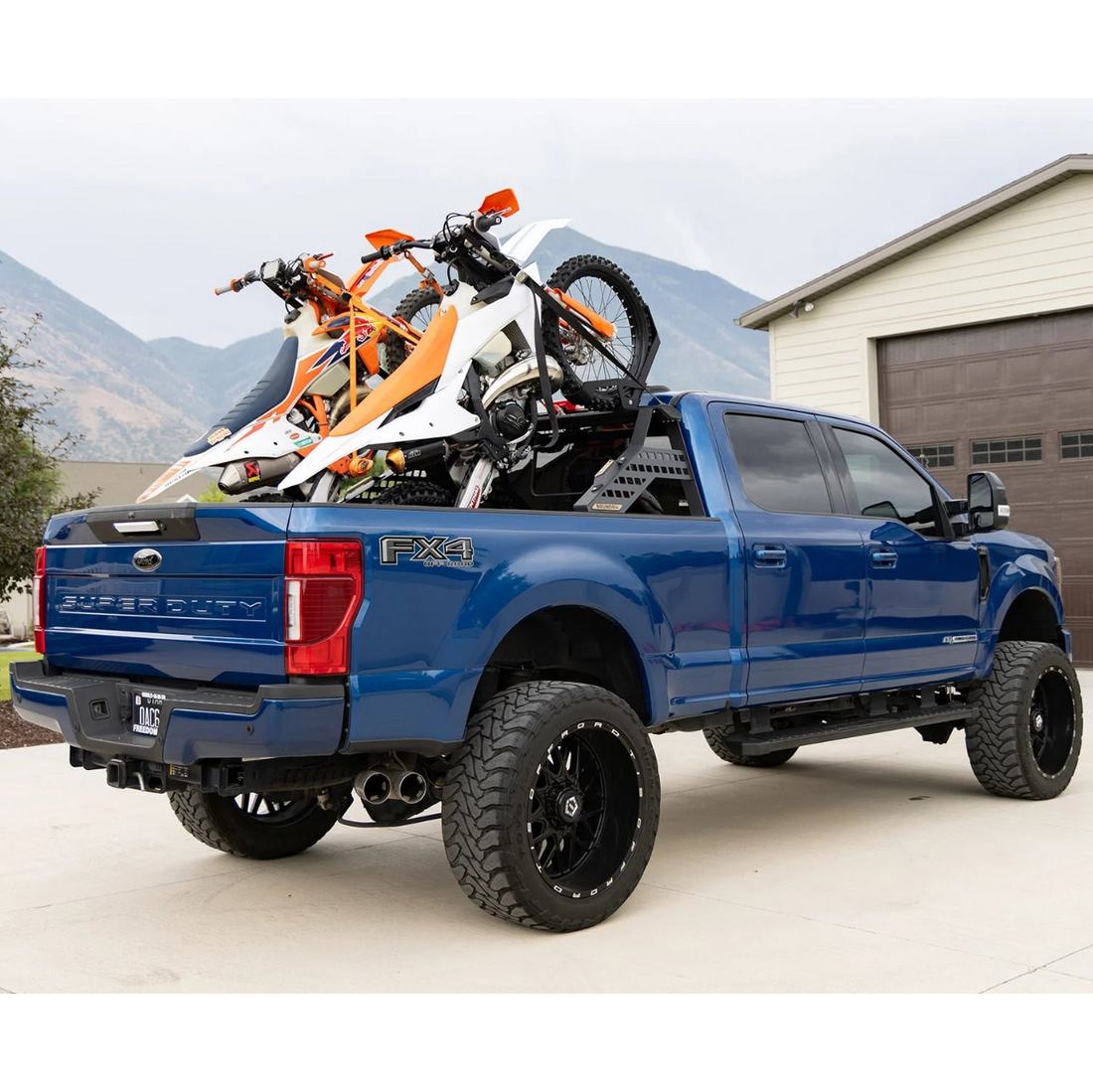 Blue pickup truck with motorcycles on the bed in a driveway.