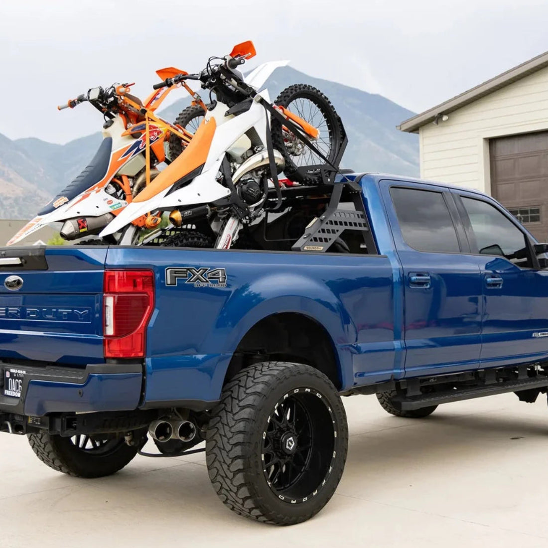Blue pickup truck with motorcycles on the bed in a driveway.