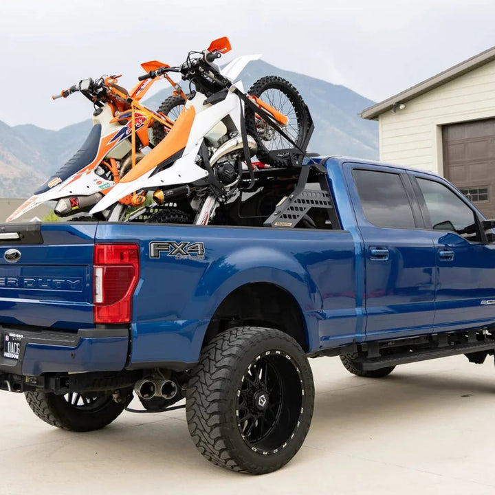 Blue pickup truck with motorcycles on the bed in a driveway.