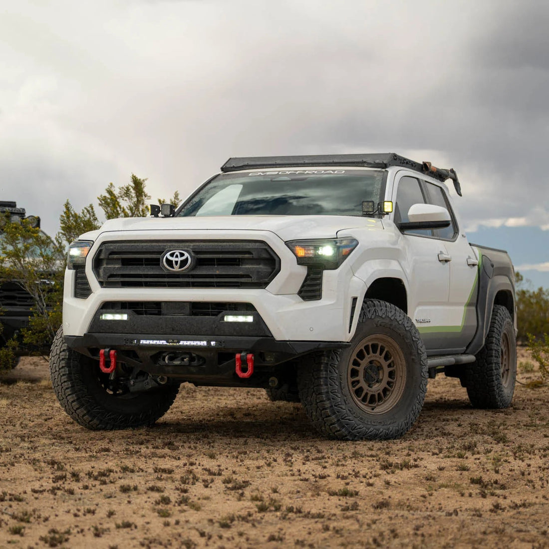 White Toyota truck in a desert landscape with another vehicle in the background.