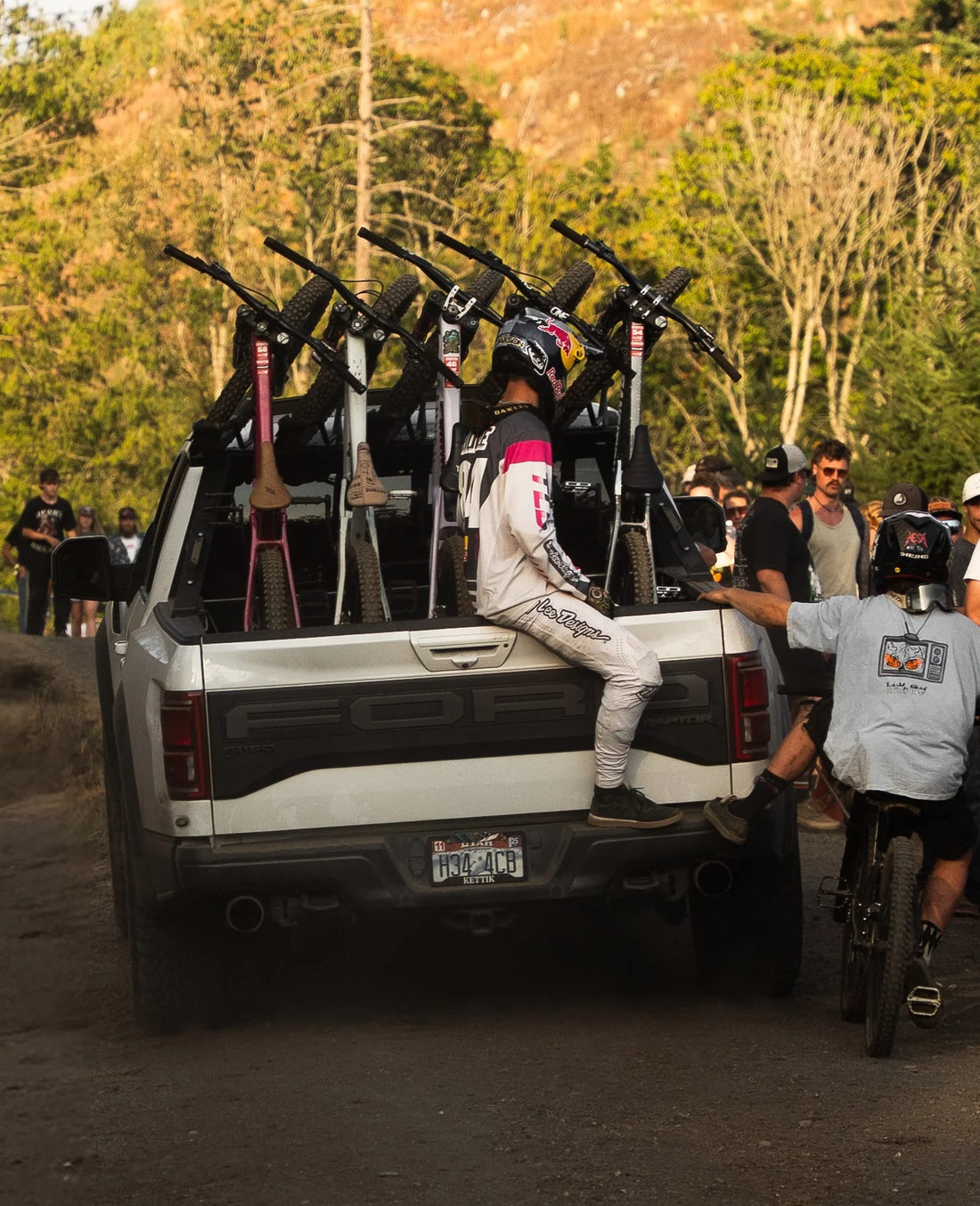 People with bicycles in a truck bed on a dirt road with trees in the background