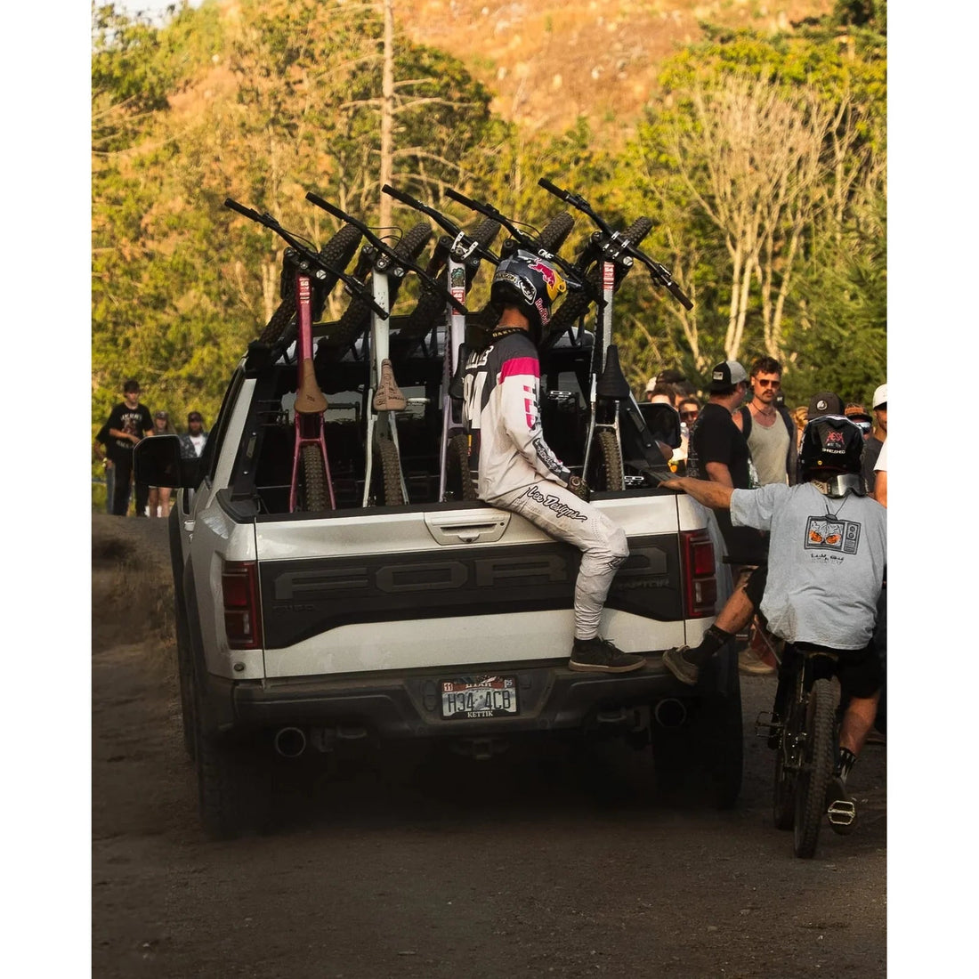 People with bicycles in a truck bed on a dirt road with trees in the background