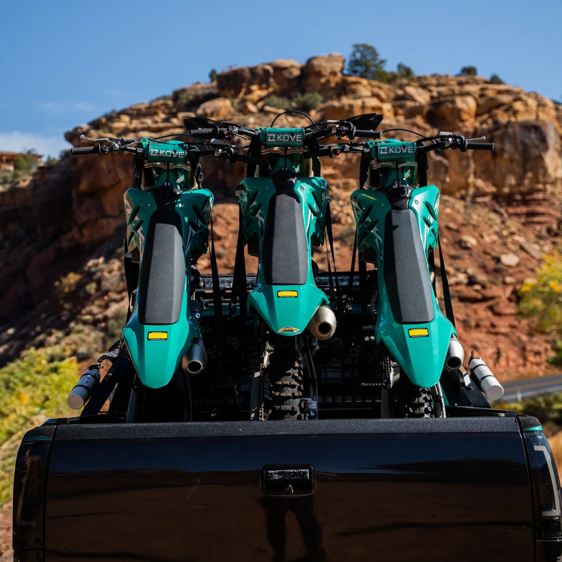 Three green off-road vehicles on a trailer with a desert landscape in the background
