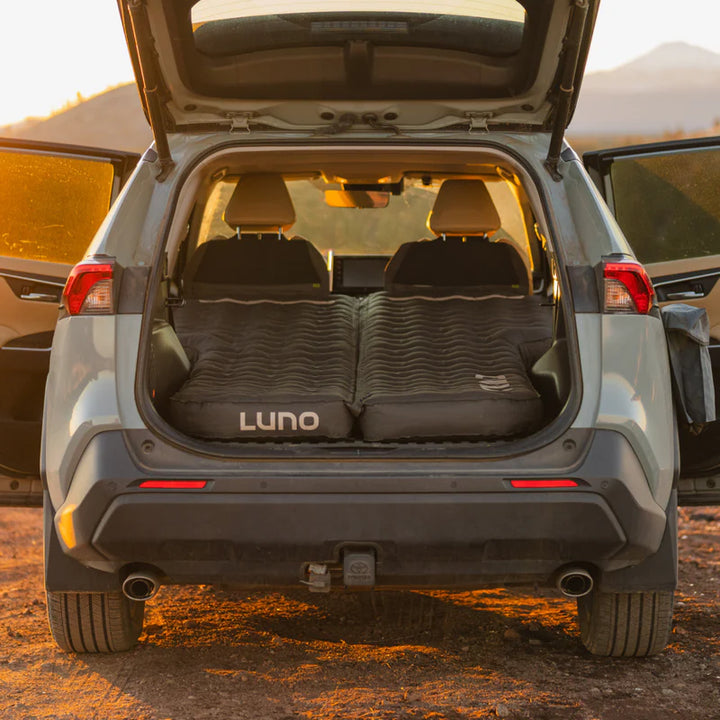 SUV with rear hatch open, outdoor air mattress set up for camping at sunset