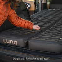 Person setting up an inflatable mattress with 'Luno' branding in a vehicle.