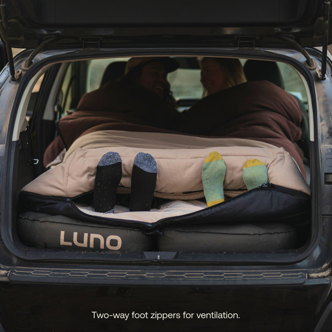 Car trunk with a sleeping pad and two people lying on it, featuring LUNO branding.