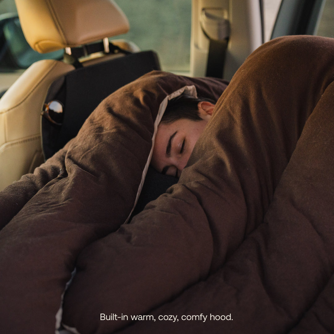 Person sleeping in a car with a brown blanket and hood