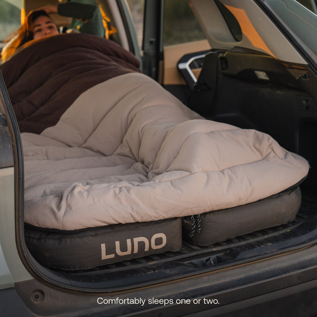Person lying on a Luno inflatable sleeping pad in the back of a car.