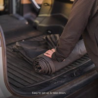 Person rolling up a mat in the back of a vehicle with text 'Easy to set up & take down.'