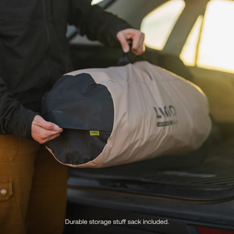 Person holding a durable storage stuff sack with Luno branding in front of a car.
