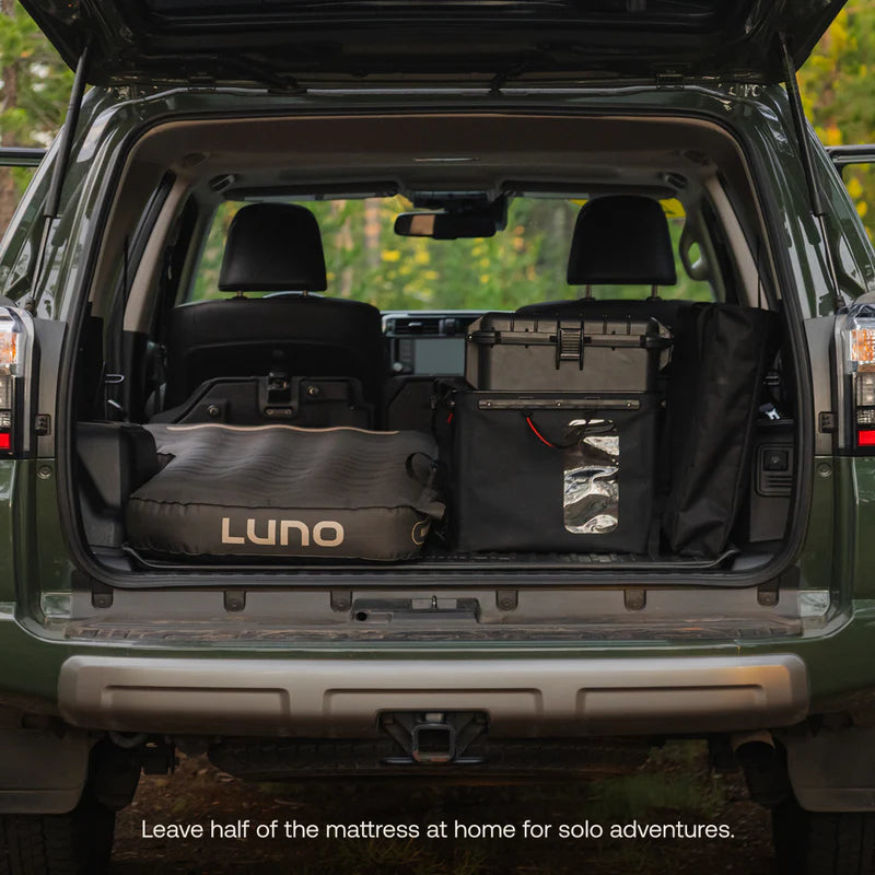 Open car trunk with camping gear, including a mattress labeled &