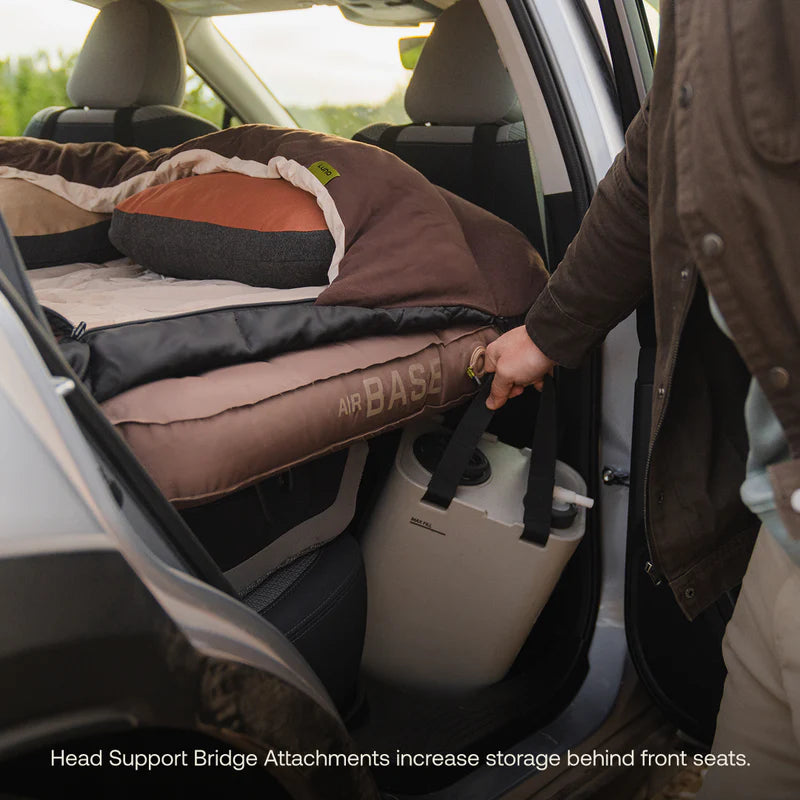 Person setting up an Air Base sleeping pad in a car with a head support bridge attachment.