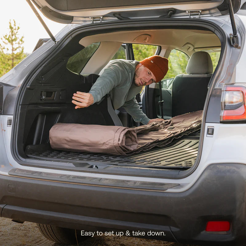 Person setting up a camping mat in the back of a car with text &