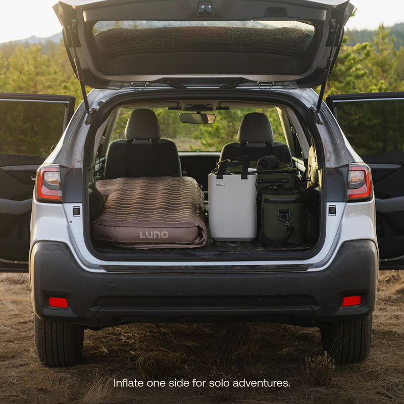 Open car trunk with camping gear including a Luno inflatable mattress and cooler.
