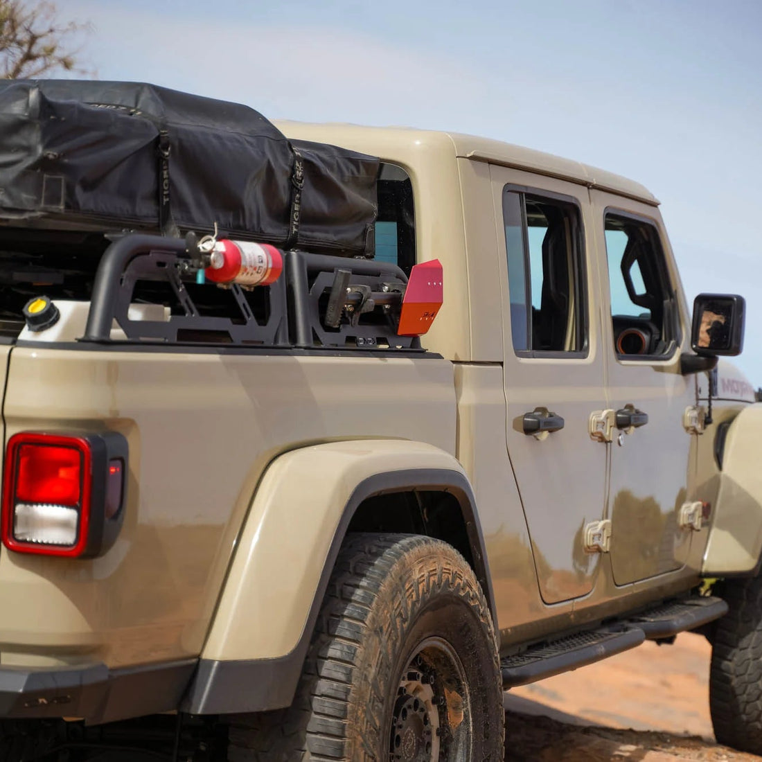 Beige Jeep Wrangler with roof rack and off-road tires on a dirt road