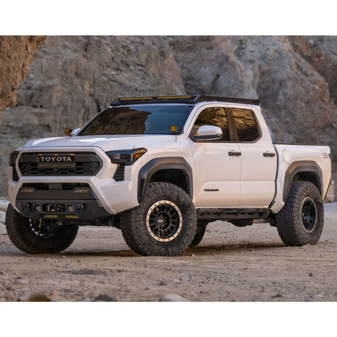 White Toyota truck in a desert setting with rocky cliffs.