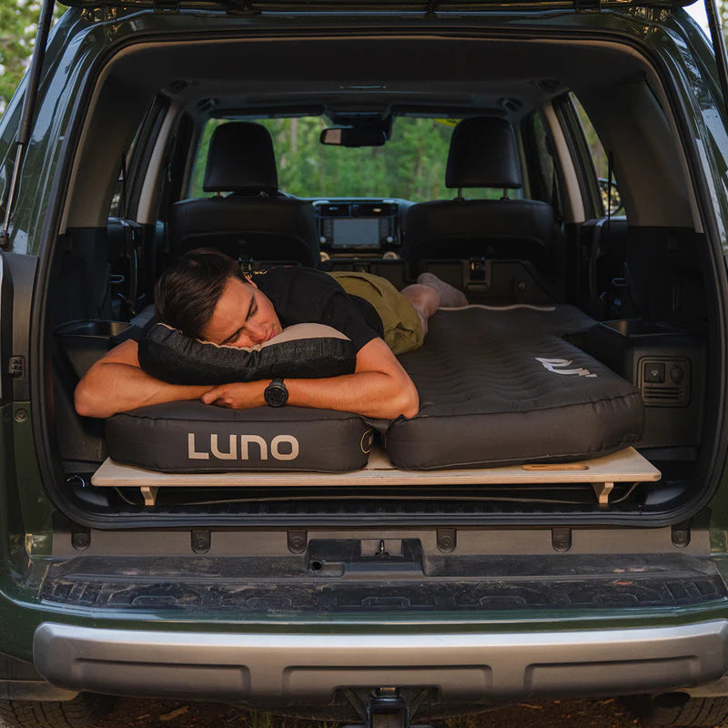 Person lying on a LUNO car bed system in the back of an open SUV.