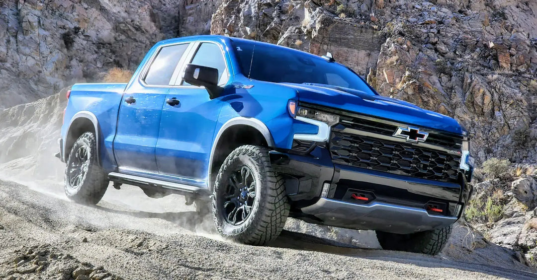 Blue Chevrolet pickup truck driving through a dusty, rocky off-road terrain.