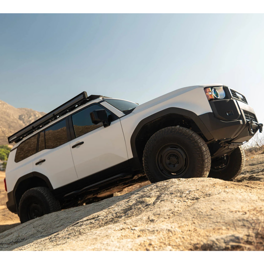 White off-road vehicle with black roof rack on a rocky terrain